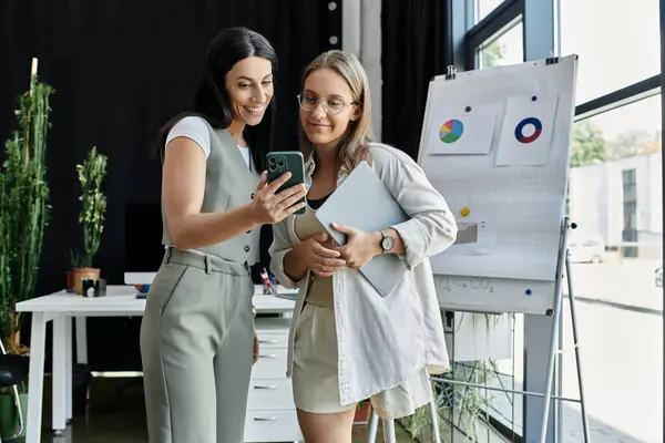 Two women analyze data for a startup on a phone in a modern office — Stock Photo
