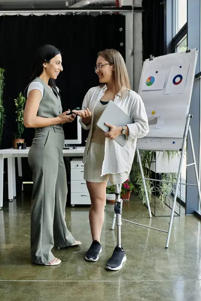Two women in a modern office, one holding a tablet, discuss ideas and plans. — Stock Photo