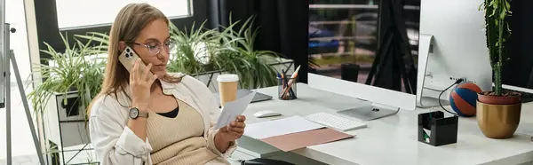 A woman talks on the phone while reviewing documents at a desk. — Stock Photo