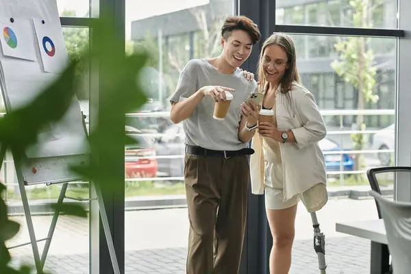Colleagues, one with prosthetic leg, share laugh over coffee while looking at phone — Stock Photo