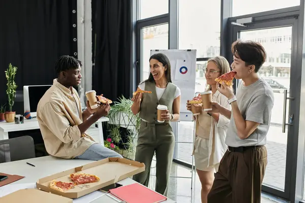 Un gruppo di quattro colleghi si gode una pausa pizza e caffè in un ambiente ufficio contemporaneo. — Foto stock