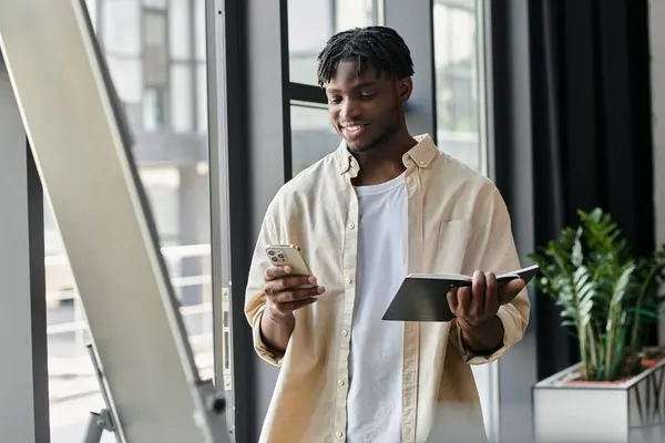 Joven, con portátil y teléfono, contempla cuidadosamente el teléfono inteligente en la oficina moderna - foto de stock