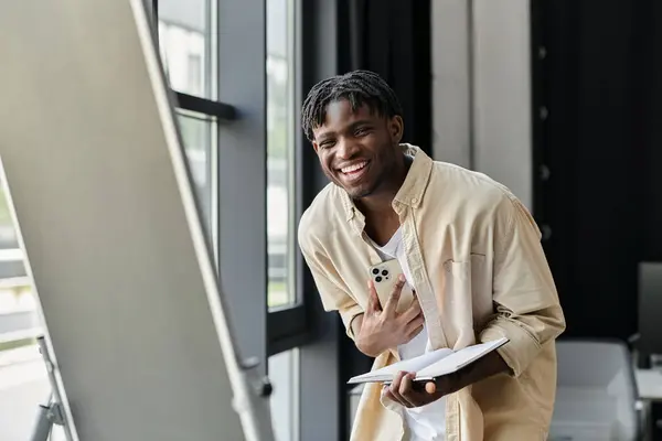 Junger Mann lächelt mit Notizbuch und Smartphone und diskutiert neue Idee im modernen Büro — Stockfoto