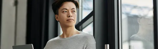 A young man, sitting in a modern office, gazes out the window, contemplating his startup dreams. — Stock Photo