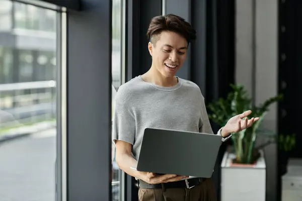 Young man smiles, gestures, discussing with colleagues, laptop in hand — Stock Photo