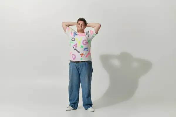 Confident individual in studio with white shirt and colorful letters, arms behind head — Stock Photo
