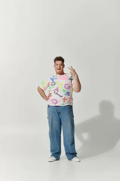 A queer person in a white shirt with colorful graffiti and blue jeans poses with a peace sign. — Stock Photo