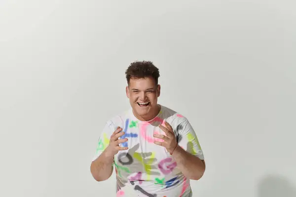 A queer person smiles brightly, wearing a white t-shirt with colorful abstract designs. — Stock Photo