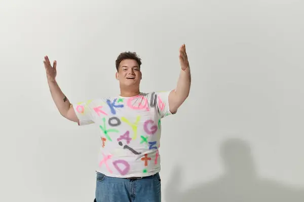 Queer person with short brown hair, big smile, white t-shirt with colorful letters, arms raised in joy — Stock Photo