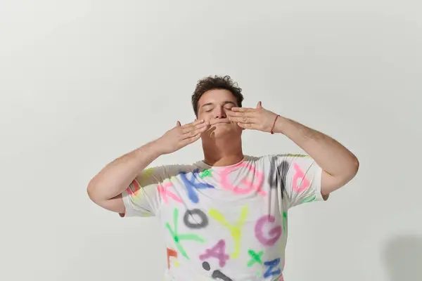 A queer person in a colorful shirt closes their eyes with hands raised in a peaceful pose. — Stock Photo