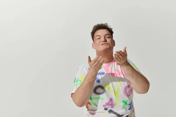 A queer person in a vibrant, colorful shirt poses confidently against a white backdrop. — Stock Photo