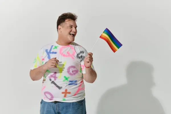 Un uomo con una camicia colorata sorride mentre sventola una bandiera arcobaleno. — Foto stock