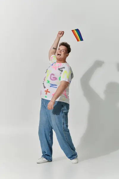 Una persona queer con un atuendo elegante lanza una bandera de arco iris en el aire, sonriendo ampliamente. — Stock Photo