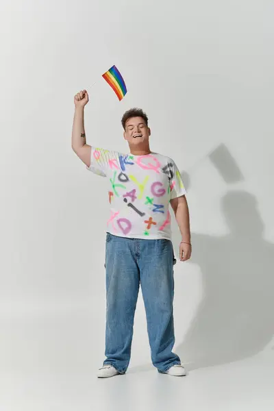 A young man smiles joyfully, holding a rainbow flag aloft. — Stock Photo