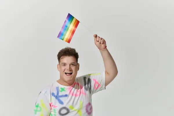Una persona queer alza una bandiera arcobaleno con un'espressione gioiosa. — Foto stock