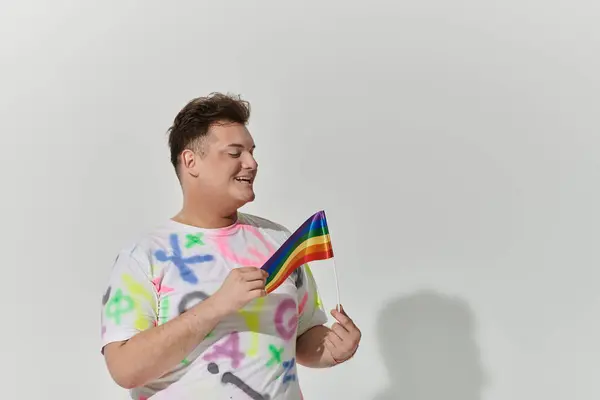 Una persona queer con una camisa colorida sostiene una bandera del arco iris, sonriendo brillantemente. — Stock Photo