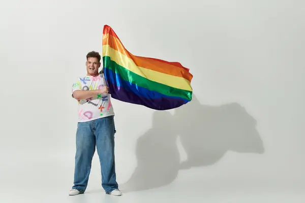 Una persona gay gioiosa sventola una bandiera arcobaleno su uno sfondo bianco. — Stock Photo