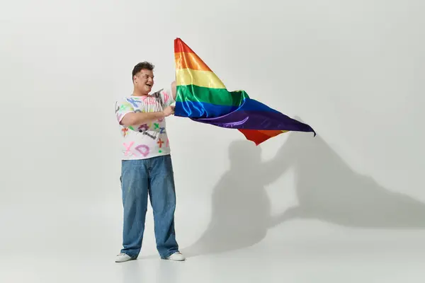 Una persona queer con un atuendo elegante sostiene una bandera de arco iris, sonriendo brillantemente. — Stock Photo
