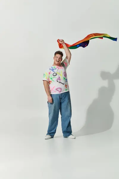 Una persona queer in una t-shirt colorata tiene una bandiera arcobaleno e sorride. — Foto stock