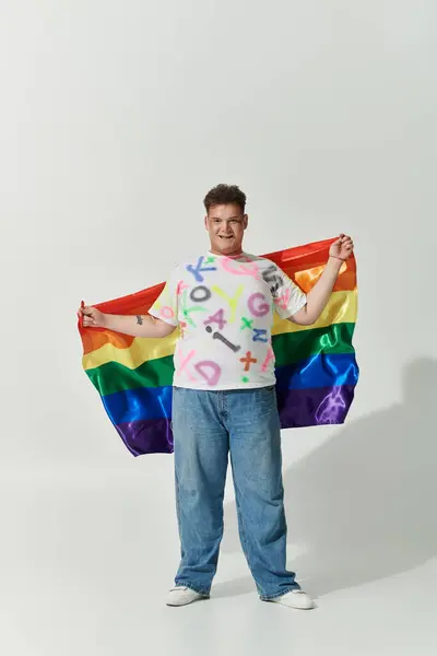 Una giovane persona queer in t-shirt bianca e jeans sorride brillantemente mentre tiene in mano una bandiera arcobaleno. — Foto stock