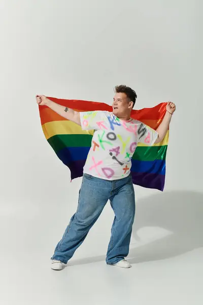 A queer person wearing a colorful shirt and jeans holds a rainbow flag. — Stock Photo