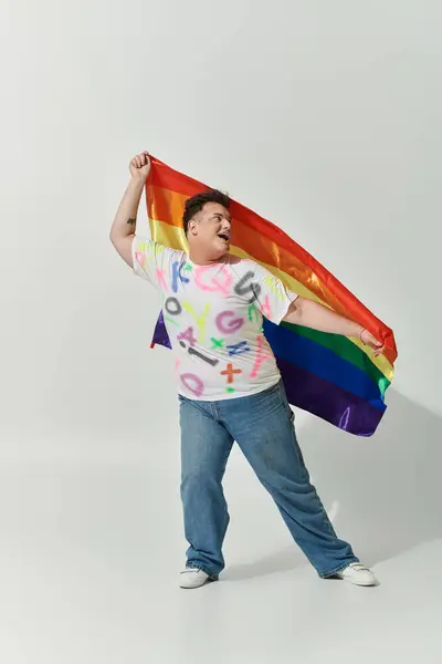 Una persona queer in abiti colorati tiene una bandiera arcobaleno, sorridendo brillantemente. — Foto stock