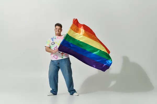 A queer person in stylish clothing holds a rainbow flag proudly. — Stock Photo