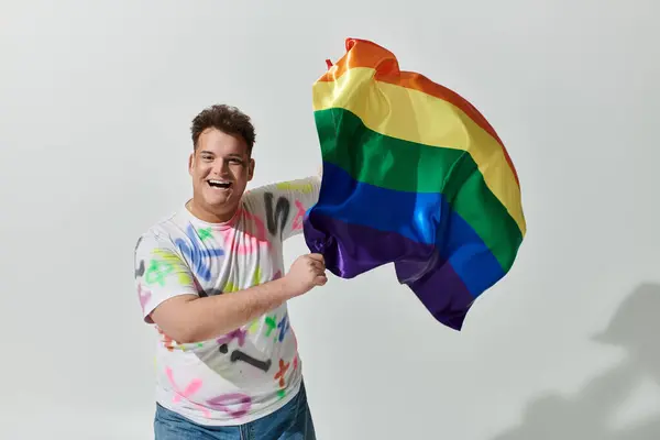 Ein Mann lächelt strahlend, als er eine Regenbogenfahne in die Höhe hält. — Stockfoto