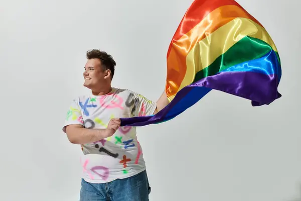 Une personne queer tient un drapeau arc-en-ciel et sourit, exprimant leur joie et leur fierté. — Photo de stock