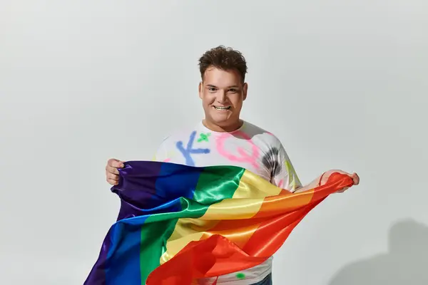 Una persona queer sorride mentre tiene una bandiera arcobaleno. — Foto stock