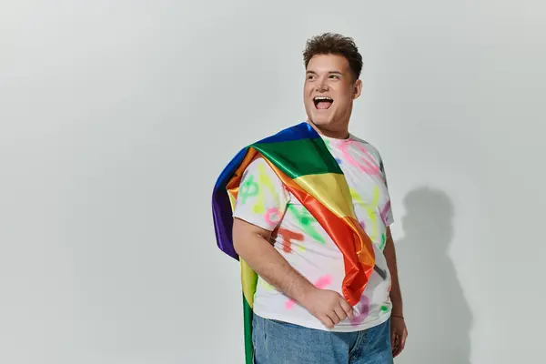 A smiling individual in stylish clothing draped in a rainbow flag. — Stock Photo