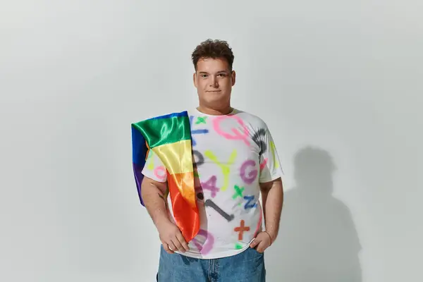 Una persona queer con una bandera del arco iris cubierta sobre su hombro, con una camiseta colorida. — Stock Photo