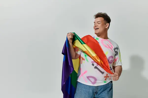 Una persona queer sorridente posa con una bandiera arcobaleno in un ambiente di studio. — Foto stock