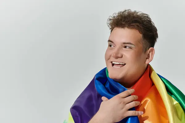 Un uomo sorride ampiamente mentre tiene una bandiera arcobaleno intorno alle spalle. — Foto stock