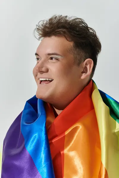 Una persona queer avvolta in una bandiera arcobaleno sorride brillantemente. — Foto stock