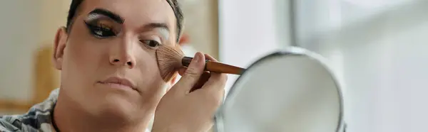 Uma pessoa queer aplica maquiagem com um pincel, olhando atentamente para seu reflexo em um espelho. — Fotografia de Stock