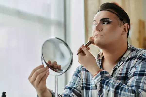 A queer person applies makeup in front of a mirror, focusing on their face. — Stock Photo