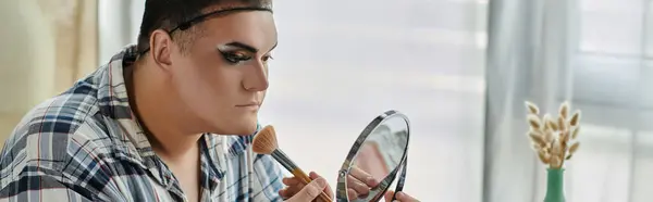 A queer person in stylish attire applies makeup in front of a mirror. — Stock Photo