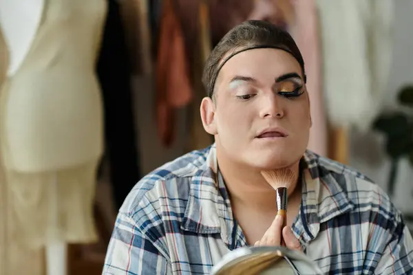 A queer person in stylish attire applies makeup in front of a mirror. — Stock Photo