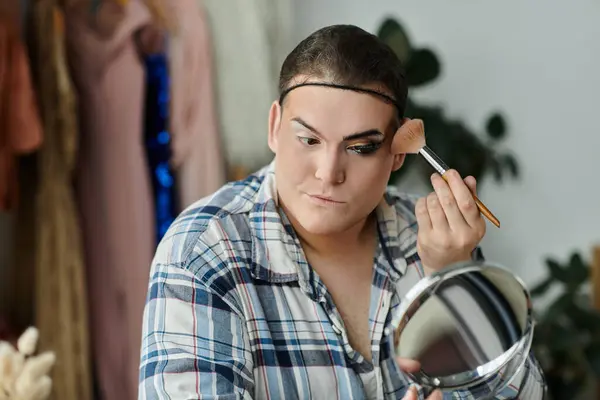 A queer person applies makeup in front of a mirror, focusing on their reflection. — Stock Photo