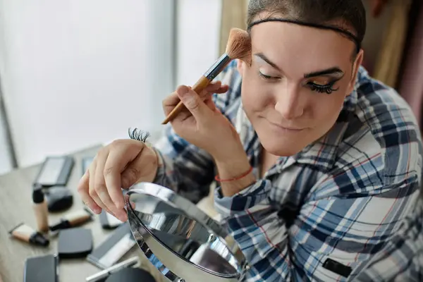 A queer person applies makeup while looking into a mirror. — Stock Photo