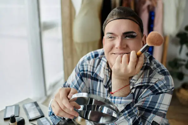 A queer person applies makeup, smiling and holding a brush and a mirror. — Stock Photo
