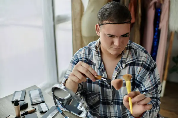 A queer person applies makeup while looking in a mirror, surrounded by a collection of beauty products. — Stock Photo