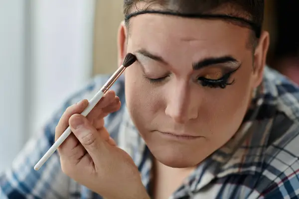 A queer person applies eyeshadow with a makeup brush. — Stock Photo