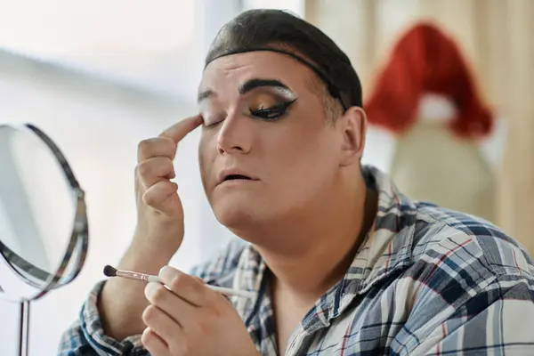 Queer person focused on reflection wearing plaid shirt applies makeup in mirror — Stock Photo