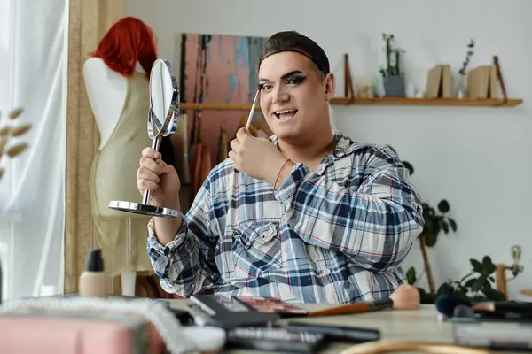 A queer person applies makeup while looking into a mirror, surrounded by various cosmetics and tools. — Stock Photo