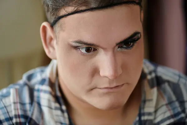 Una persona queer con un trucco audace guarda in basso, la loro espressione illeggibile. — Foto stock