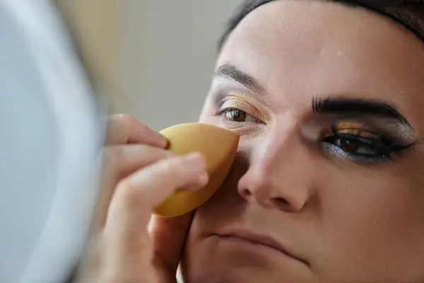 A queer person is getting their makeup done, focusing on the eyes. — Stock Photo