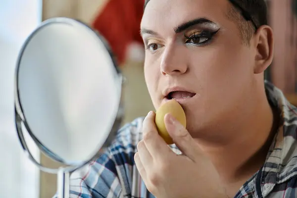 A queer person applies makeup while looking in the mirror. — Stock Photo