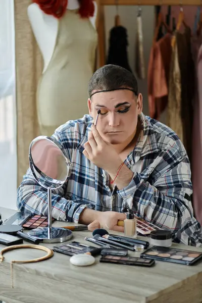 Une personne queer applique le maquillage tout en regardant dans le miroir, entouré d'un éventail d'outils de beauté. — Photo de stock